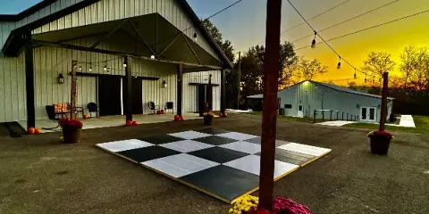 Exterior view of a metal barn wedding venue with an outdoor dance floor and string lights at sunset.