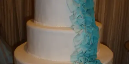 A four-tier white wedding cake decorated with cascading blue fondant ruffles.
