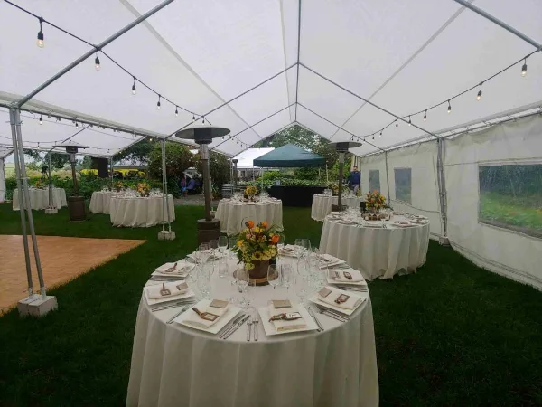 An outdoor event tent set up with round tables, white table linens, and a wooden dance floor.