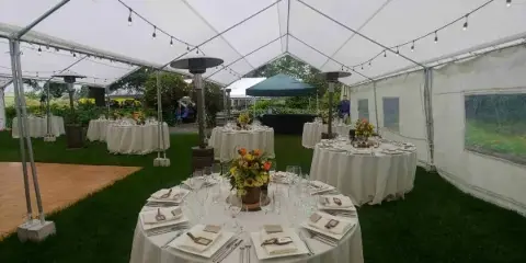 An outdoor event tent set up with round tables, white table linens, and a wooden dance floor.