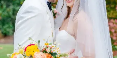 A bride and groom smiling and embracing outdoors, with the bride holding a vibrant bouquet.