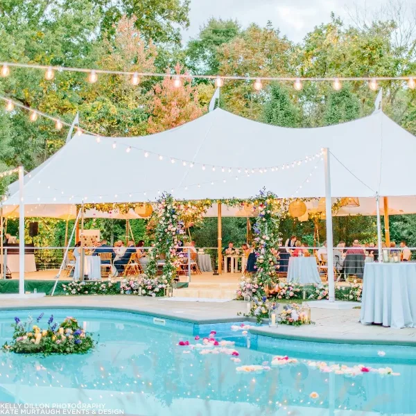A white event tent set up outdoors for a wedding reception with floral decorations and string lights.