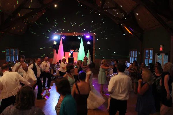A bride and guests dancing at a wedding reception under colorful stage lights with a DJ booth in the background.