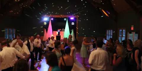 A bride and guests dancing at a wedding reception under colorful stage lights with a DJ booth in the background.
