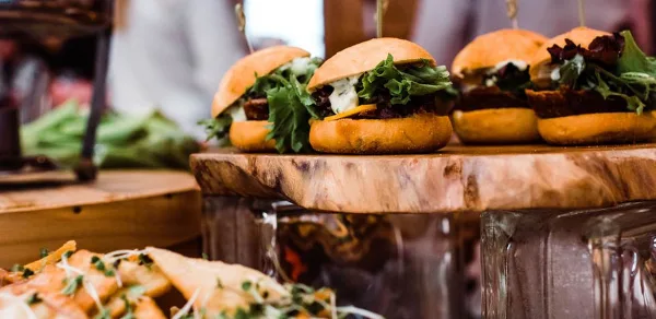A wooden serving board holding several sliders with lettuce and cheese, with a side of potato wedges in the foreground.