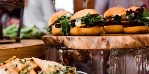 A wooden serving board holding several sliders with lettuce and cheese, with a side of potato wedges in the foreground.