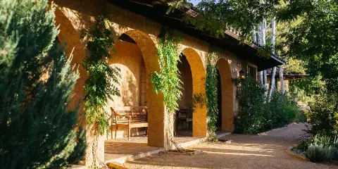 Exterior view of a Mediterranean-style estate venue featuring arched walkways, stucco walls, and lush greenery.