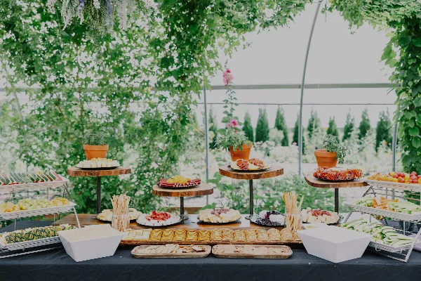 A catering table set with a charcuterie board, fresh fruit, and pastries under a floral canopy.