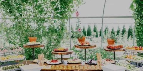 A catering table set with a charcuterie board, fresh fruit, and pastries under a floral canopy.