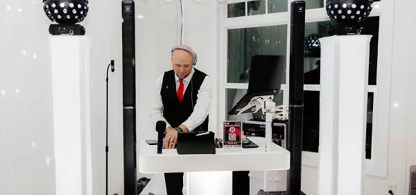 A professional DJ wearing a vest and red tie operating a mixing console at an event venue.