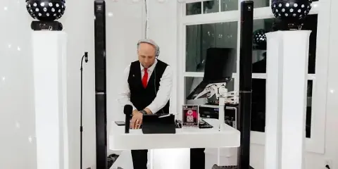 A professional DJ wearing a vest and red tie operating a mixing console at an event venue.
