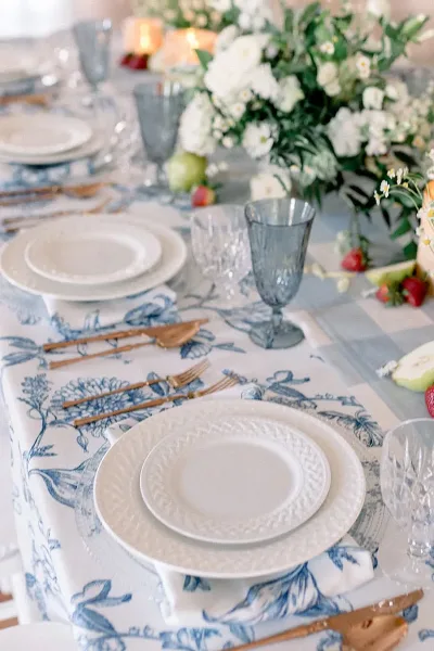 A close-up of an elegant event table setting featuring white plates, blue patterned linens, and glassware.