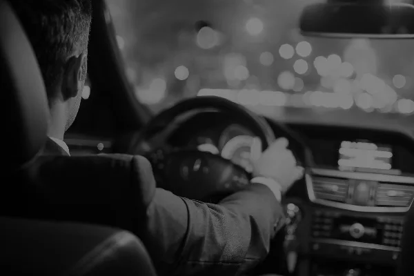 A professional chauffeur in a suit driving a luxury vehicle at night.
