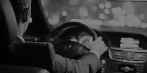 A professional chauffeur in a suit driving a luxury vehicle at night.