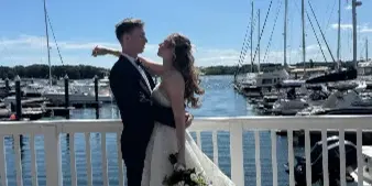 A bride and groom embracing on a wooden dock at a marina with sailboats in the background.