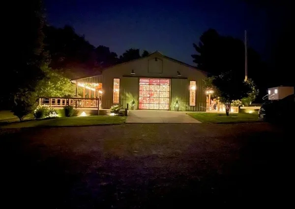 Exterior view of a rural event center building at night with illuminated windows and a paved entrance.