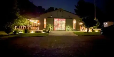 Exterior view of a rural event center building at night with illuminated windows and a paved entrance.