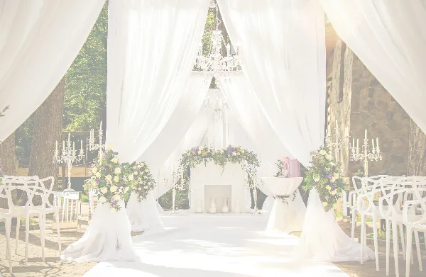 A wedding ceremony setup featuring a white draped arch, floral arrangements, and white chairs arranged in an outdoor venue.