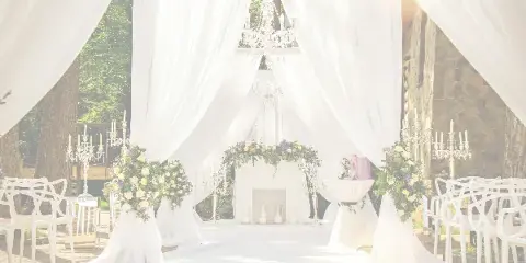 A wedding ceremony setup featuring a white draped arch, floral arrangements, and white chairs arranged in an outdoor venue.