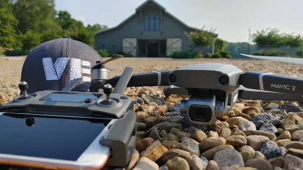 A DJI Mavic 2 drone and controller with a VE Videography cap on a gravel surface in front of a house.