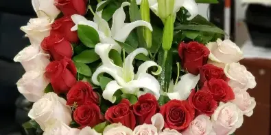 A tall floral arrangement featuring red, white, and blush roses with white lilies and greenery on a table.
