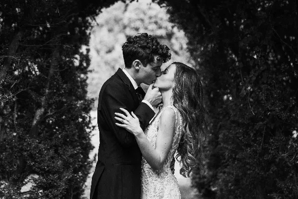 Black and white photograph of a bride and groom kissing outdoors.