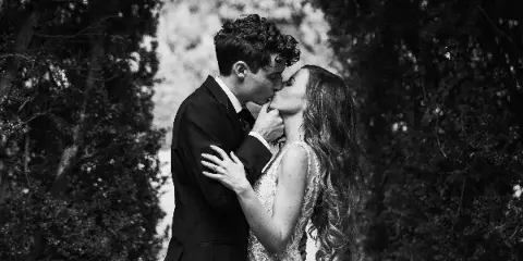 Black and white photograph of a bride and groom kissing outdoors.
