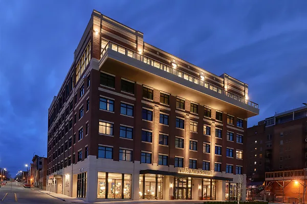Exterior view of The Merrill Hotel building at dusk, showing its brick facade and illuminated entrance.