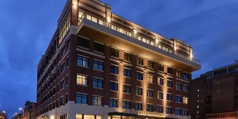 Exterior view of The Merrill Hotel building at dusk, showing its brick facade and illuminated entrance.