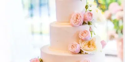A four-tier white wedding cake decorated with cascading pink and white roses on a silver stand.
