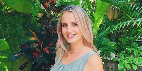 Portrait of Diana, the founder of Happily Maui'd, standing in front of tropical foliage.