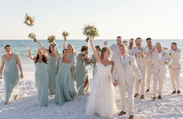 A wedding party on a beach holding floral bouquets and boutonnieres.