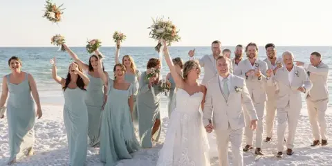 A wedding party on a beach holding floral bouquets and boutonnieres.