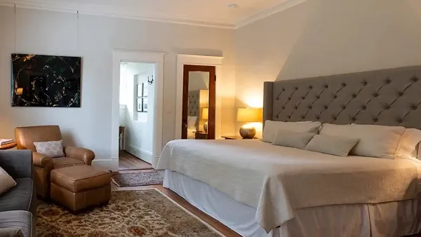 A guest bedroom featuring a large bed with a tufted headboard, leather armchair, and wall art.
