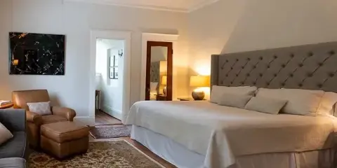 A guest bedroom featuring a large bed with a tufted headboard, leather armchair, and wall art.