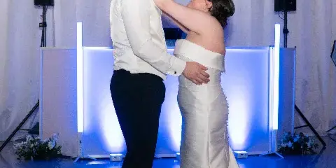 A bride and groom dancing in front of a DJ booth featuring professional speakers and vertical LED light bars.