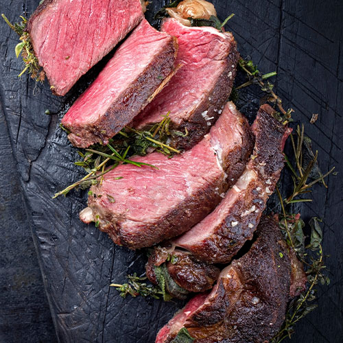 Sliced cooked steak garnished with fresh herbs on a dark wooden serving board.