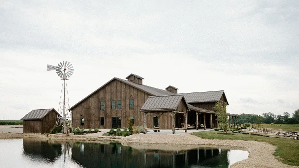 A rustic wooden barn wedding venue with a pond and windmill on a farm.