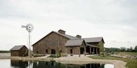A rustic wooden barn wedding venue with a pond and windmill on a farm.