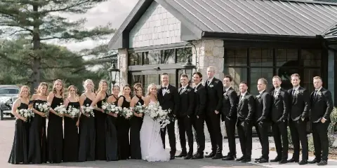 A wedding party posing in front of The Clubhouse venue building.