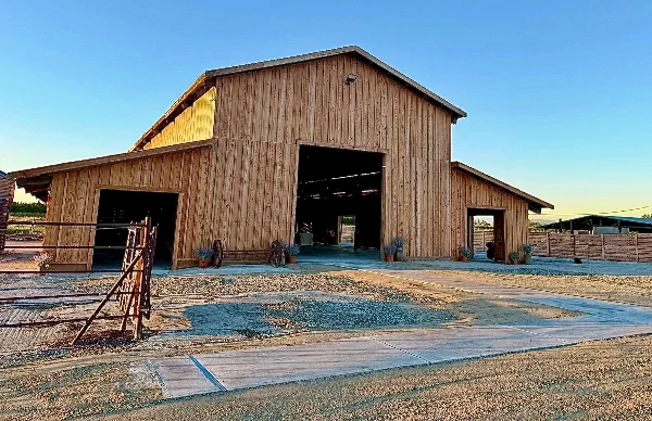 Exterior view of a large wooden barn wedding venue with open doors and a gravel driveway.