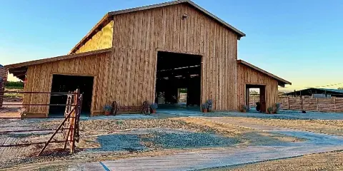 Exterior view of a large wooden barn wedding venue with open doors and a gravel driveway.