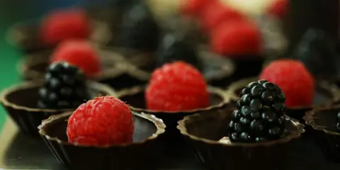 A tray of chocolate cups topped with fresh raspberries and blackberries.