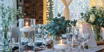 A close-up view of a formal dining table setting featuring glassware, candles, and floral arrangements.
