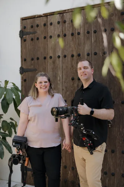 A man and a woman standing together holding professional video cameras and a gimbal stabilizer.
