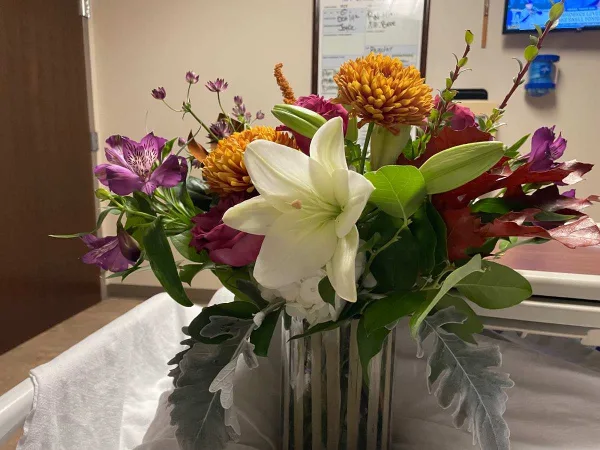 A vibrant floral arrangement with white lilies, purple alstroemeria, and orange chrysanthemums in a clear glass vase.