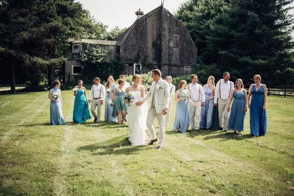A wedding party posing in a grassy field in front of a rustic barn.