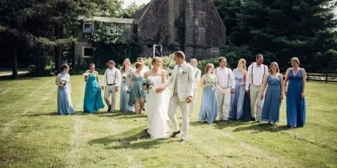 A wedding party posing in a grassy field in front of a rustic barn.