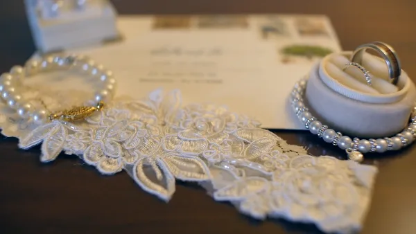 Close-up cinematic shot of wedding rings, lace fabric, and pearls on a dark surface.
