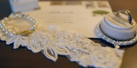 Close-up cinematic shot of wedding rings, lace fabric, and pearls on a dark surface.